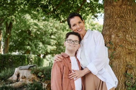 glückliche Frau mittleren Alters umarmt Sohn mit Down-Syndrom im Park