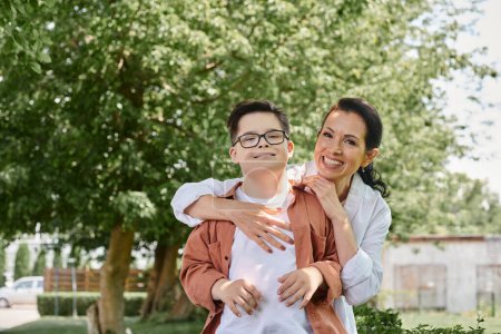 Foto de Alegre mujer de mediana edad abrazando sonriente hijo con síndrome de Down en el parque, amor incondicional - Imagen libre de derechos