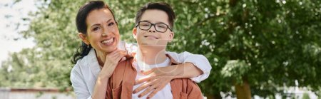 Téléchargez les photos : Souriant femme d'âge moyen étreignant son fils avec le syndrome du duvet dans le parc, connexion émotionnelle, bannière - en image libre de droit