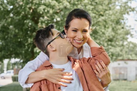 Téléchargez les photos : Enfant avec le syndrome du duvet embrasser souriant mère d'âge moyen pendant la sortie du parc, moments heureux - en image libre de droit
