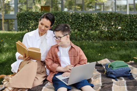 happy middle aged woman reading book near son with down syndrome using laptop in park