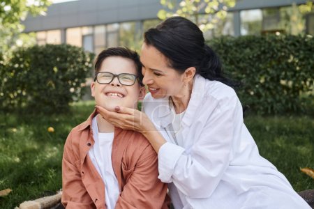 glückliche Frau mittleren Alters berührt Gesicht ihres Sohnes mit Down-Syndrom im Park, bedingungslose Liebe