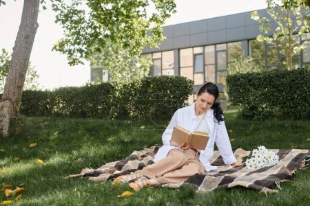 middle aged woman in casual attire reading novel while sitting on blanket in park, quality time
