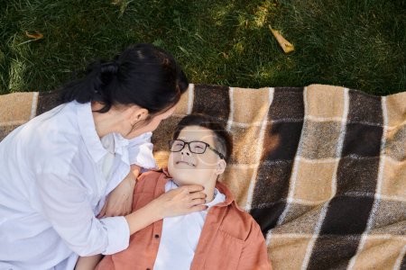 Foto de Vista superior de la madre cerca de hijo feliz con síndrome de Down en la manta en el parque, el amor incondicional - Imagen libre de derechos