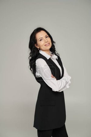 moderne und stilvolle Geschäftsfrau mittleren Alters in Bürokleidung lächelt in die Kamera auf grau