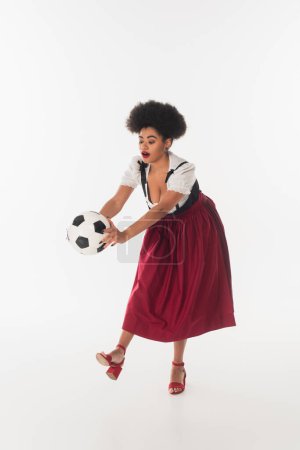 african american oktoberfest waitress in traditional bavarian dirndl playing football on white