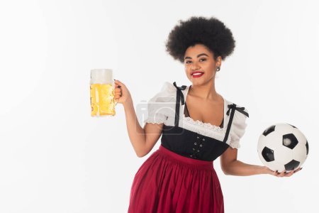 african american oktoberfest waitress with soccer ball and mug of lager beer with foam on white
