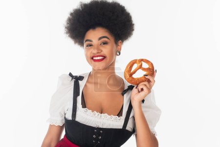 young african american waitress in traditional bavarian costume holding delicious pretzel on white
