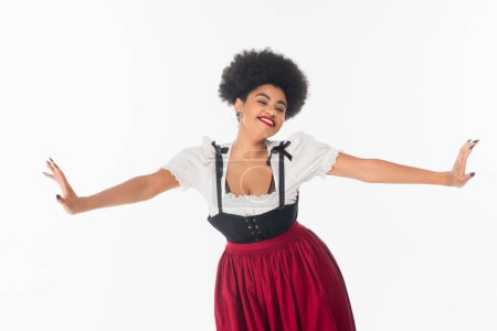 alegre camarera afroamericana en traje bavariano tradicional con las manos extendidas sobre blanco