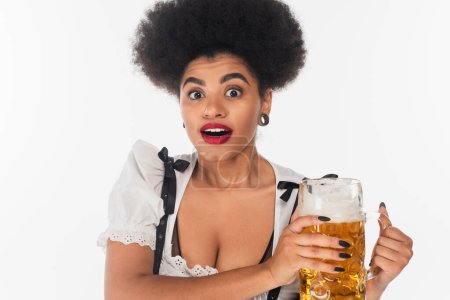 überraschte afrikanisch-amerikanische Kellnerin im traditionellen bayerischen Dirndl mit Bierkrug auf weißem Grund