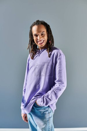 fröhlicher junger afrikanisch-amerikanischer Mann in lässigem lila Sweatshirt, der in die Kamera blickt und lächelt