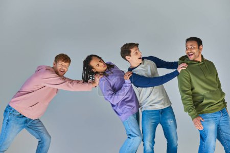 Foto de Cuatro hombres felices sonrientes en traje urbano casual teniendo gran tiempo sobre fondo gris, diversidad cultural - Imagen libre de derechos