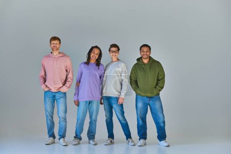 Foto de Cuatro jóvenes alegres en trajes casuales callejeros mirando y sonriendo a la cámara, diversidad cultural - Imagen libre de derechos