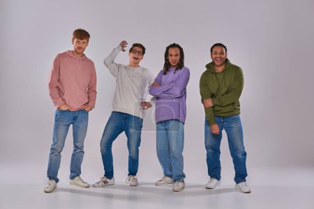 czterech młodych wielokulturowych mężczyzn w luźnych strojach stojących i śmiejących się z aparatu fotograficznego, różnorodność kulturowa
