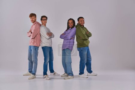 Photo for Four young men standing back to back and smiling at camera on grey backdrop, cultural diversity - Royalty Free Image