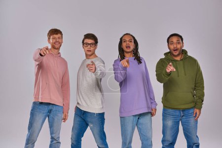 Foto de Jóvenes hombres guapos de pie y señalando con los dedos a la cámara sobre fondo gris, diversidad cultural - Imagen libre de derechos