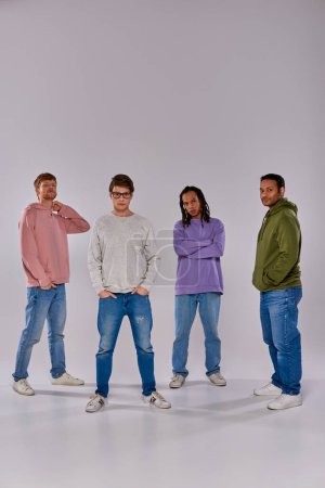 Foto de Cuatro jóvenes amigos en trajes de moda casual de pie mirando a la cámara en el fondo gris, la diversidad - Imagen libre de derechos