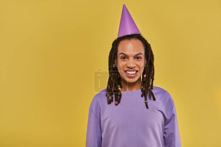 fröhlicher afrikanisch-amerikanischer Mann mit Geburtstagsmütze und durchbohrter Lippe, der in die Kamera lächelt, Geburtstag