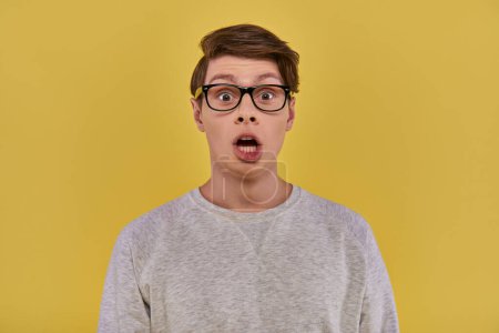 überraschter junger Mann in lässiger bequemer Kleidung und Brille blickt mit offenem Mund in die Kamera