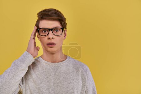 Schockierter Mann in weißem Sweatshirt berührt Brille und öffnet leicht den Mund auf gelbem Hintergrund