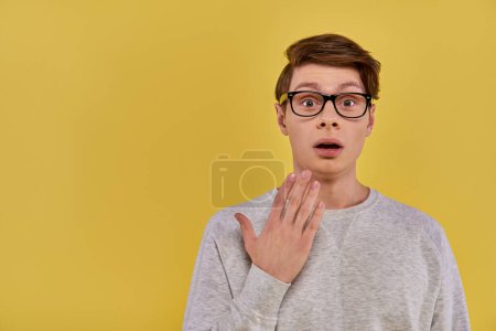 verblüffter junger Mann im weißen Outfit mit schwarzer Brille, die den Mund überraschend öffnet, die Hand nah am Mund