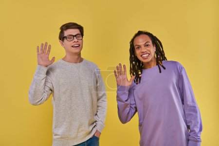 Photo for Two cheerful friends in purple and white sweatshirts waving and smiling at camera, diversity - Royalty Free Image