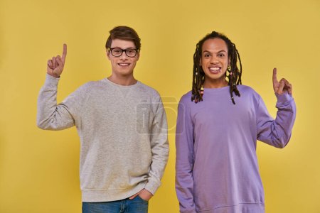 two multicultural men in casual outfits standing with fingers pointing up, cultural diverse