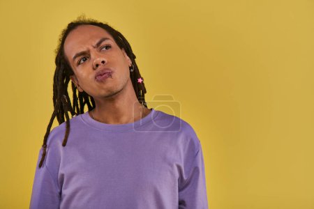 close up thoughtful young man in purple outfit with dreadlocks looking away on yellow backdrop