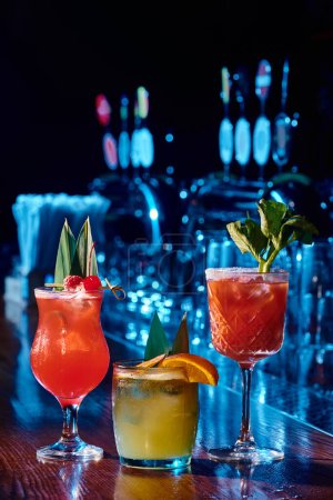 three different refreshing cocktails on bar counter with bar on backdrop, concept