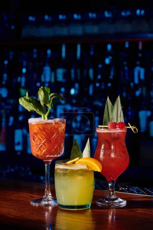 three refreshing cocktails with fruit and plant decorations with bar on background, concept