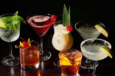 köstliche erfrischende Reihe von ästhetischen Cocktails mit Garnierungen auf schwarzem Hintergrund, Konzept