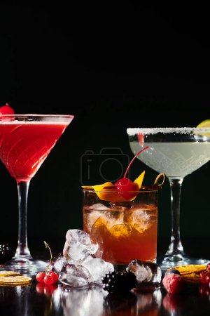 Durstlöschende Cocktails garniert mit Kirschen und Limetten auf schwarzem Hintergrund, Konzept