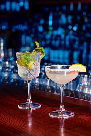 Elegante Gläser leckerer Cocktails mit Dekoration und Bar im Hintergrund, Konzept