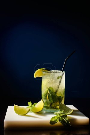 Photo for Thirst quenching cold mojito garnished with mint leaves and lime on black backdrop, concept - Royalty Free Image