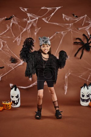 Mädchen im schwarzen Outfit mit Eimer voller Süßigkeiten und Laternen auf braunem Hintergrund, Halloween