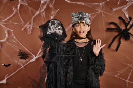 surprised preteen girl in faux fur attire holding skeleton toy, Halloween concept, close up