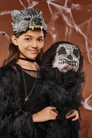 Téléchargez les photos : Portrait de sourire preteen fille tenant effrayant jouet d'Halloween sur fond brun, Halloween, gros plan - en image libre de droit