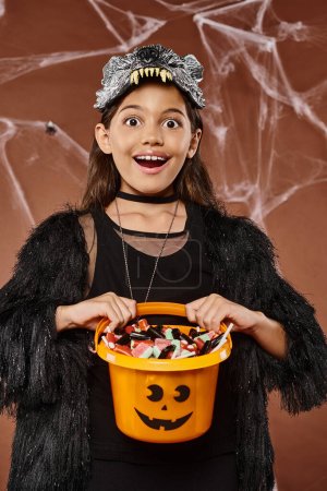 Porträt eines glücklichen Mädchens in Wolfsmaske mit einem Eimer voller Süßigkeiten, Halloween-Konzept
