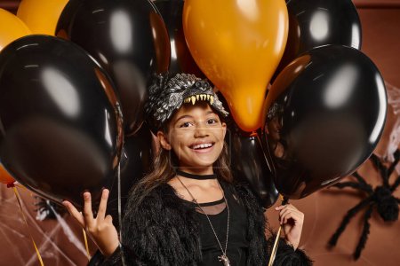Porträt eines süßen, mit schwarzen und orangefarbenen Luftballons umgebenen Mädchens, Halloween-Konzept
