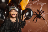 close up happy preteen girl with balloons with spider web brown backdrop, Halloween concept magic mug #676677916