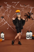 preteen girl holding pumpkin on her head with raised hands, brown backdrop with web, Halloween magic mug #676678180