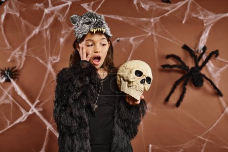 Nahaufnahme verängstigtes Frühchen mit Wolfsmaske hält Totenkopf in den Händen, Halloween-Konzept