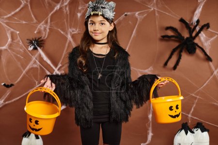 smiley kid in wolf mask with two pumpkin buckets on brown background with webs, Halloween, close up
