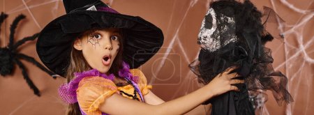 close up surprised kid in witch hat and spiderweb makeup holds scary toy, Halloween, banner