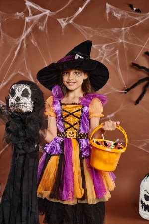 Nahaufnahme glückliches Kind mit Spinnennetz Make-up hält Eimer mit Süßigkeiten und gruseliges Spielzeug, Halloween
