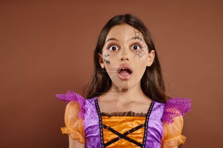Gesichtsausdruck, schockiertes Mädchen im Halloween-Kostüm, das vor braunem Hintergrund in die Kamera schaut, gruselig