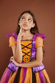thoughtful girl in colorful costume with Halloween makeup looking away on brown background, October Tank Top #676682098