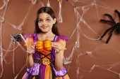 cheerful girl with spiderweb makeup in Halloween costume holding pumpkins on brown backdrop puzzle #676715512