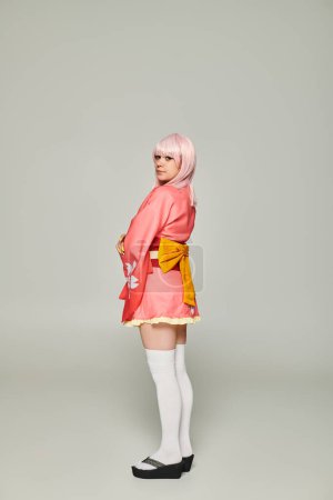 young anime style woman in blonde wig and pink kimono with yellow bow on grey, cosplay concept