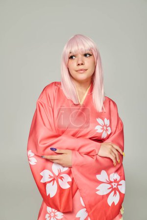 Téléchargez les photos : Femme blonde avec manucure colorée posant en kimono rose avec imprimé floral sur gris, style anime - en image libre de droit
